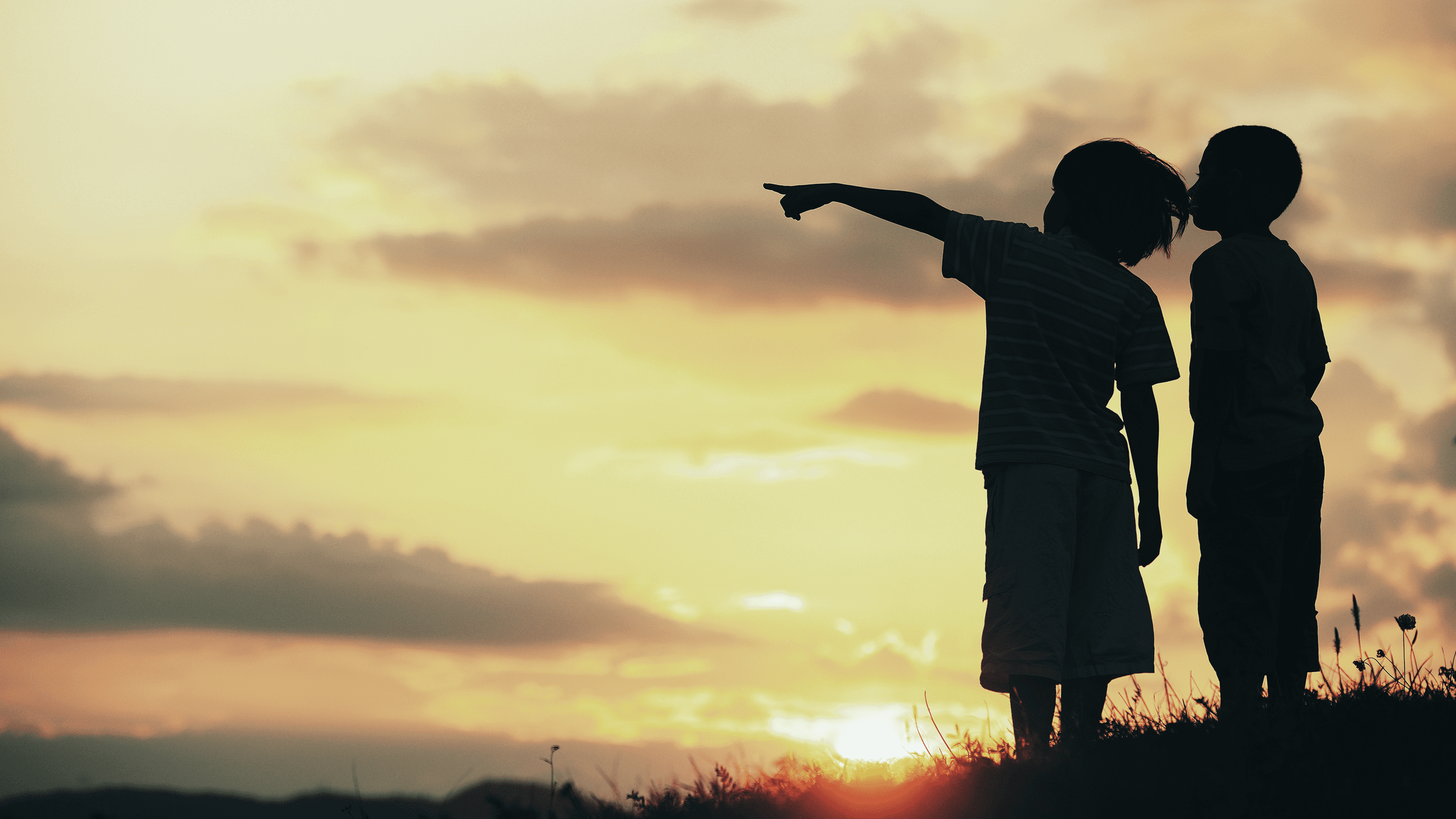 Kaksi lasta katselee horisontissa näkyvää auringonlaskua
